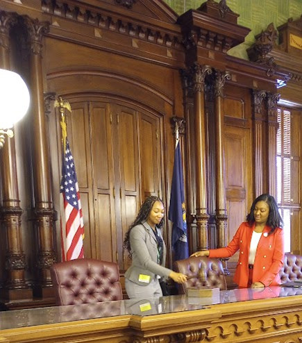 A young lady banging a gavel on an ornate desk next to a woman.